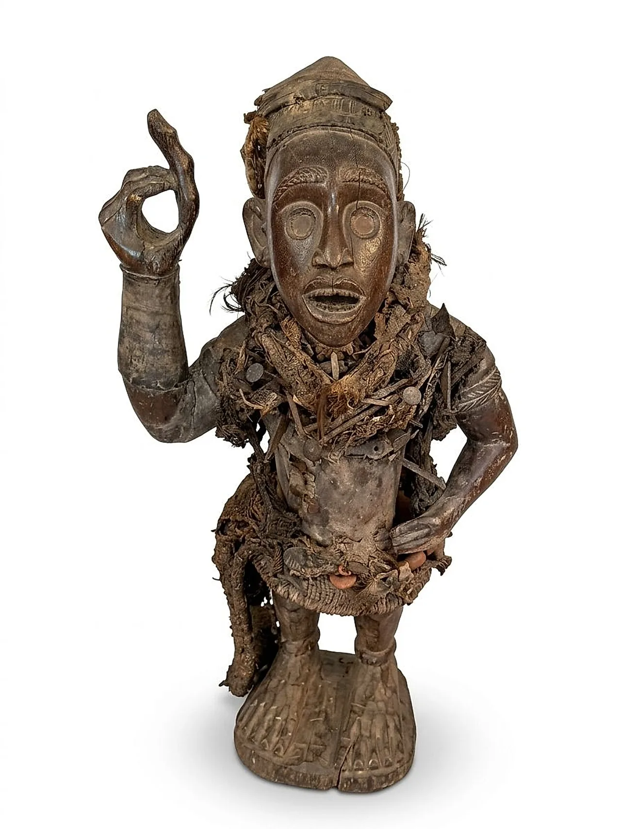 Nkisi Nkondi power figure, front view: raised hand, fitted cap and torso charged with nails, blades and fibre